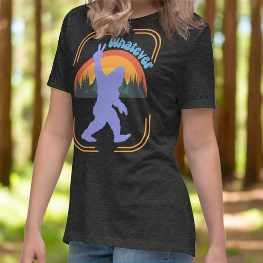 Dark Grey Sasquatch Women's T-Shirt on model turned slightly to the left. Big Foot in periwinkle against a rainbow and mountains showing a peace sign with text Whatever. Bigfoot Yeti Women's Tee