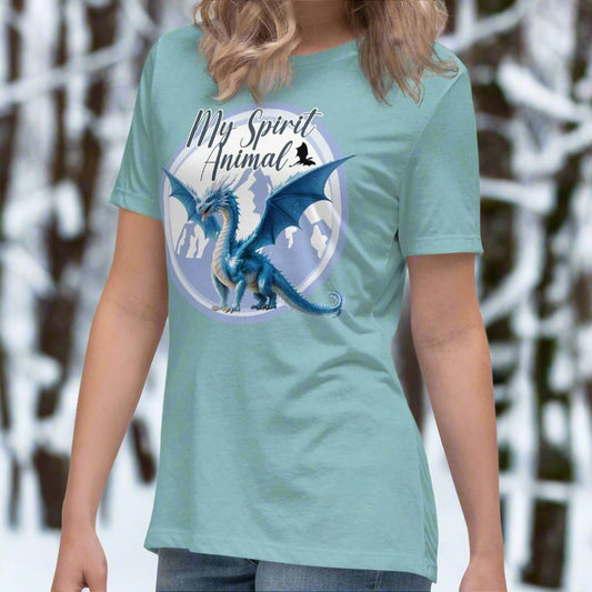 My Spirit Animal Dragon Women's Graphic Tee, front view of blue lagoon shirt, Blue Ice Dragon with wings spread standing in front of snow capped mountain range with a dragon silhouette flying above within a blue grey circle