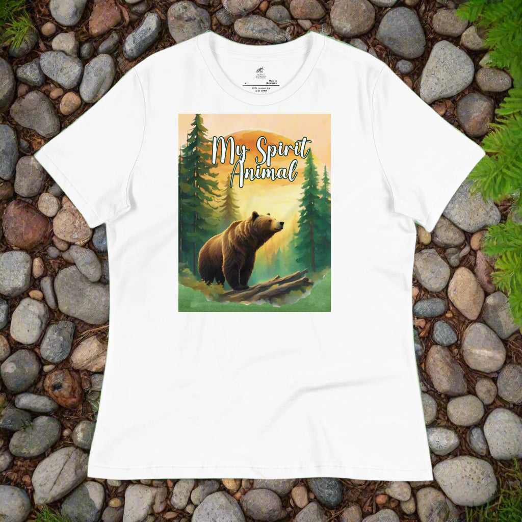 Women's My Spirit Animal Grizzly Bear T-Shirt. Front view white flay lay on rock path. Grizzly Bear paused in front of logs walking through the forest framed in a sunset. My Spirit Animal at the top between fir trees.