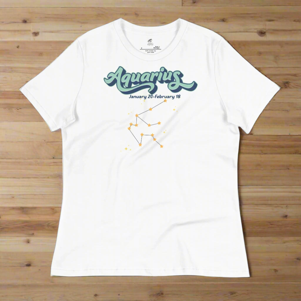 Flat lay white astrology Aquarius women's T-shirt on a wooden counter. At the top in light blue is the word Aquarius outlined in deeper blue. Below this it says January 20- February 18. Under this is the Aquarius constellation with orange yellow stars connected by a black line. Astrology Zodiac Aquarius Woman's Tee