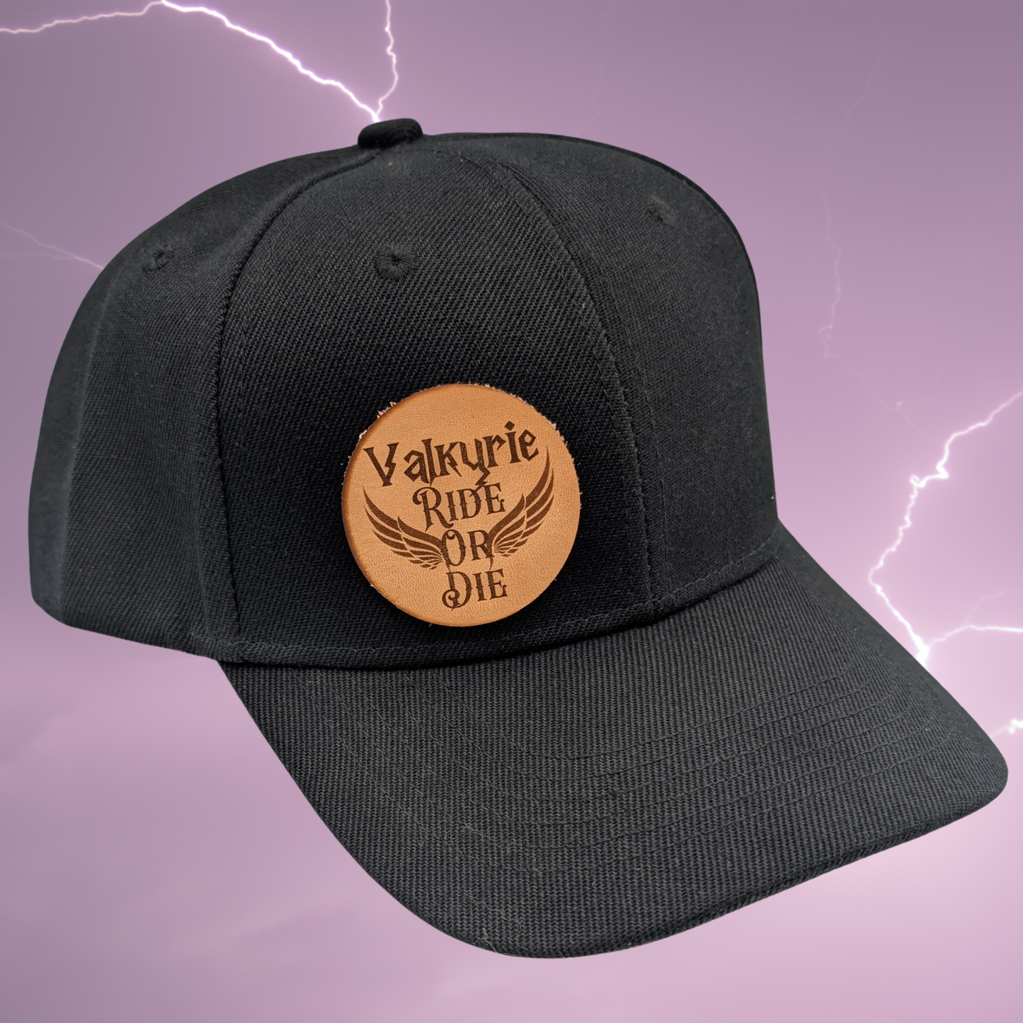 Right front view of black cotton snapback hat. On the front right side of the hat is a round leather patch. The leather patch is laser engraved with Valkyrie Ride Or Die. From the word Or wings spread out to both sides. Valkyrie Warrior Viking Hat