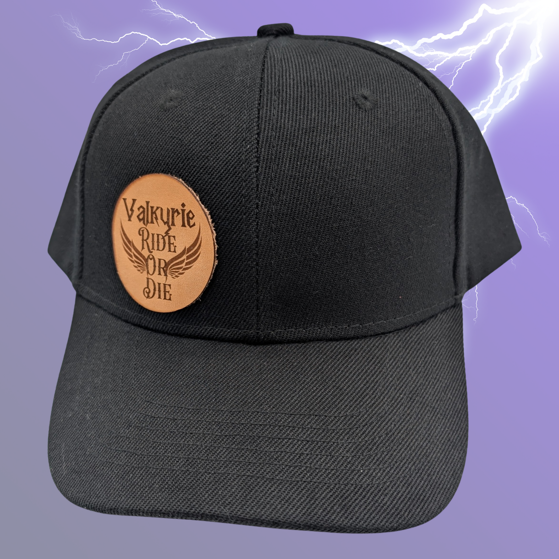 front view of black cotton snapback hat. On the front right side of the hat is a round leather patch. The leather patch is laser engraved with Valkyrie Ride Or Die. From the word Or wings spread out to both sides. Valkyrie Warrior Viking Hat