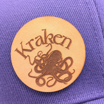 Up close view of Laser Engraved Leather Patch Text Kraken curved above the image of a Kraken. Kraken Viking Hat 