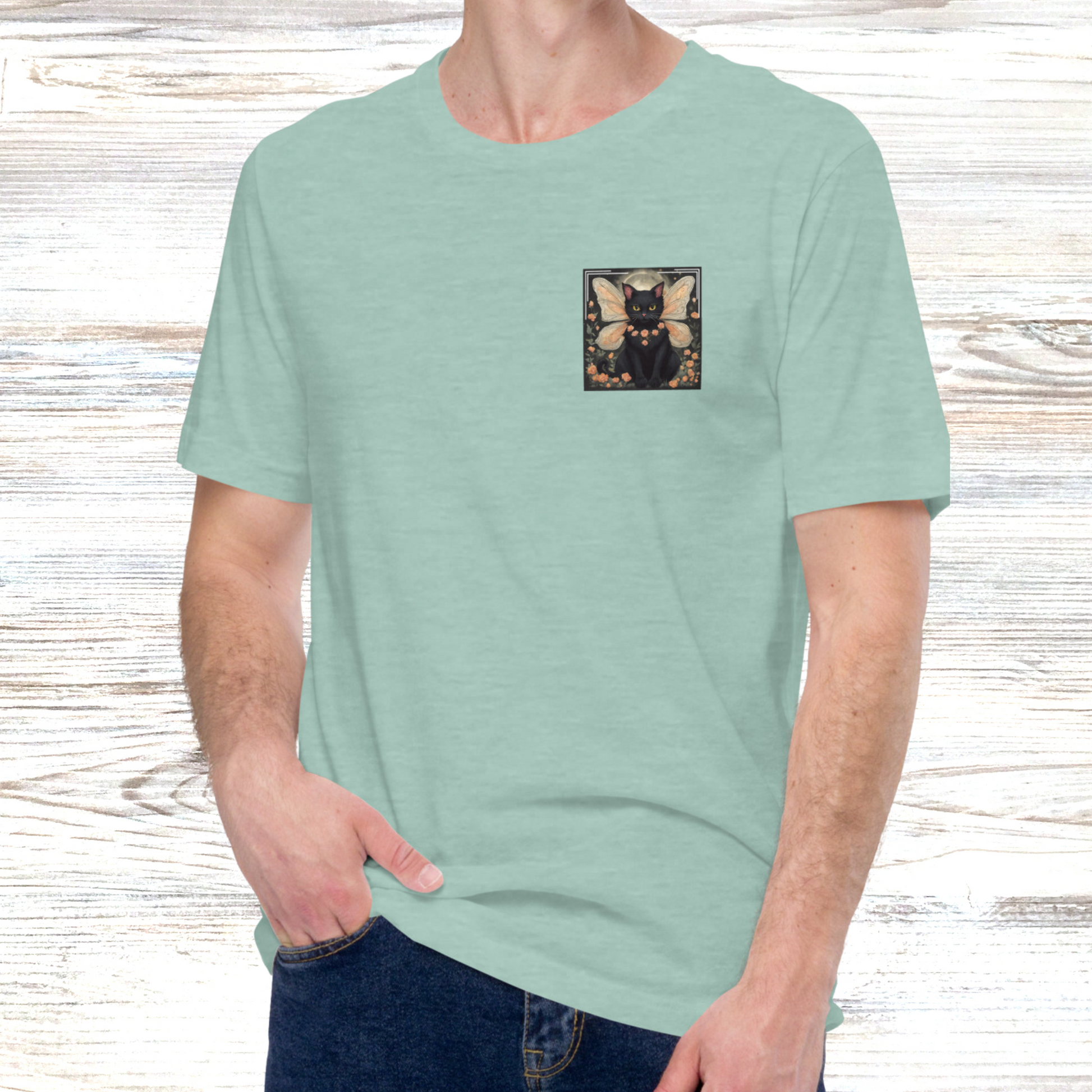 Men's Heather Prism Dusty Blue Crew Neck T-Shirt is a light green blue color. Black Fairy Cat Sitting in a field of peach roses. Framed between the black cat's fairy wings is a full moon. Black cat has yellow eyes and a garland of peach roses around it's neck. Graphic is approximately 3.5 inch square on the left upper side of the shirt.