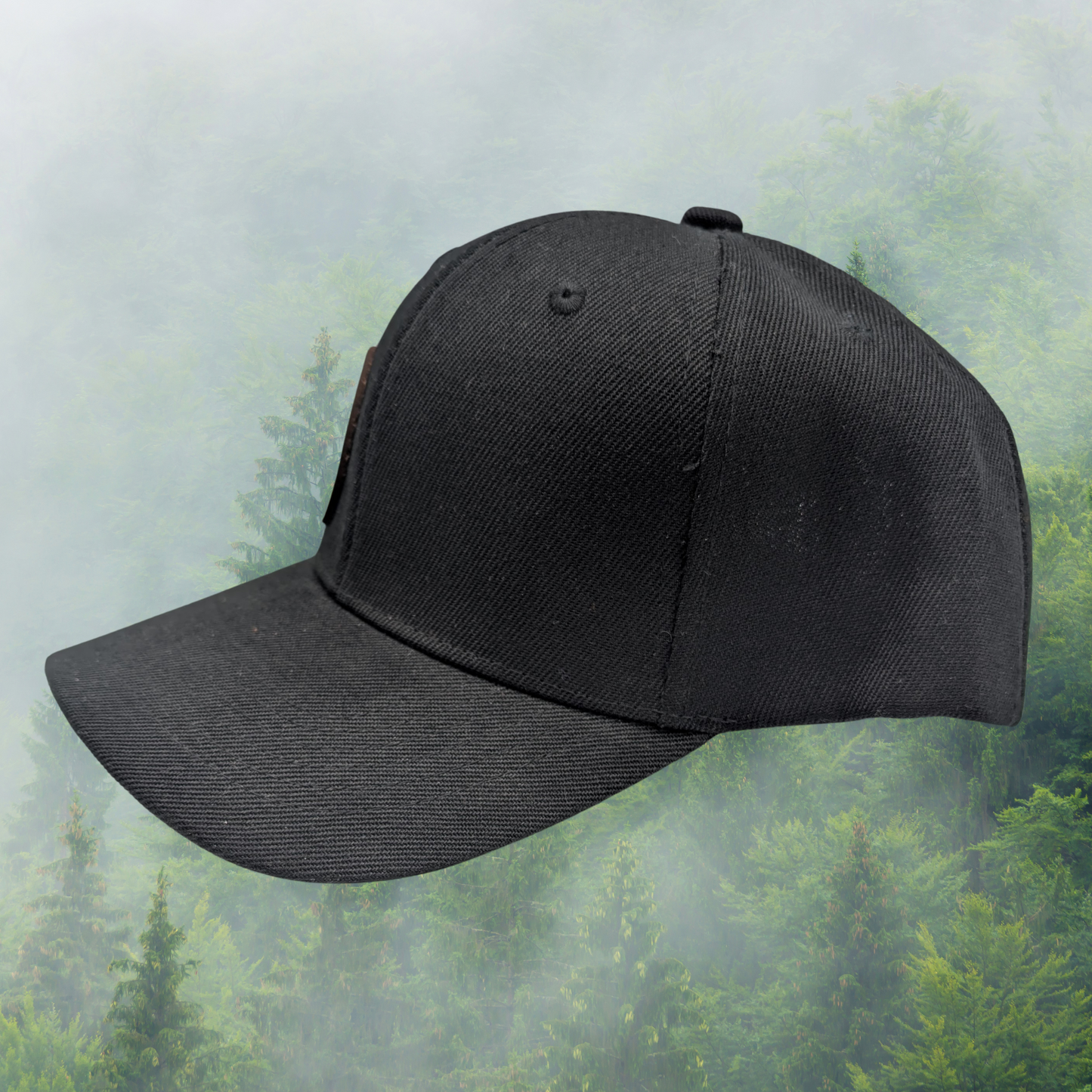 Left side view of Black Snapback Trucker Hat with a round leather laser engraved patch on the right side of the front. Leather Patch has a circle frame of a leafless tree in a with the branches reaching from the left to the right to make a circle. Ravens are in the branches and flying in the middle of the patch.