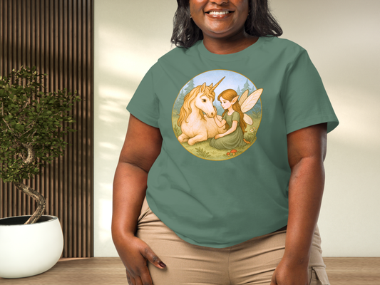 curvy model wearing a green bay Fantasy graphic tee. Graphic is a circle. Beneath a blue sky in a forest meadow a winged fairy kneels next to a unicorn while petting it. Fairy is wearing a green dress and has auburn hair.
