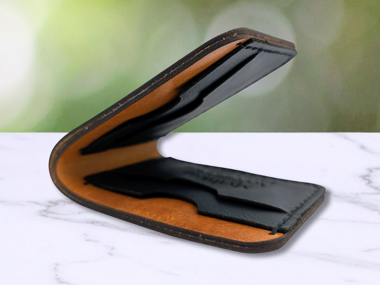 Veg Tan Handmade Leather Bi Fold Wallet. You are looking into the wallet that is slightly closed to see all 4 of the black pebbled leather card pockets. On the front of the card compartment on the bottom of the left side the Mythical Accessories Emporium logo is engraved. 