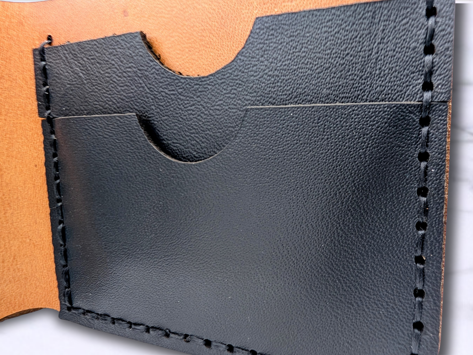 Close up of the black pebbled leather card pockets handsewn in dark waxed cord to the veg tan wallet. There are two card pockets on the left and right side of the wallet.