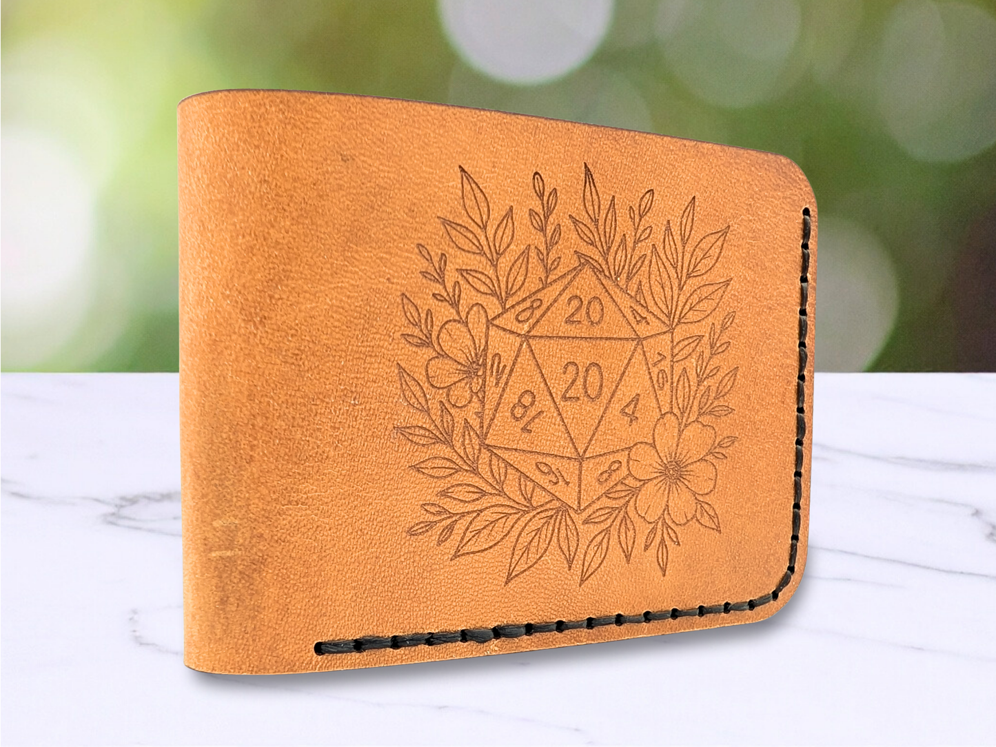 D20 veg tan wallet handmade with a D20 laser engraved on the front. The D20 is surrounded by leaves and a flower. This light brown leather bi fold wallet is dad style standing on the edge to showcase the folded side of the leather wallet with a view of the front engraving.