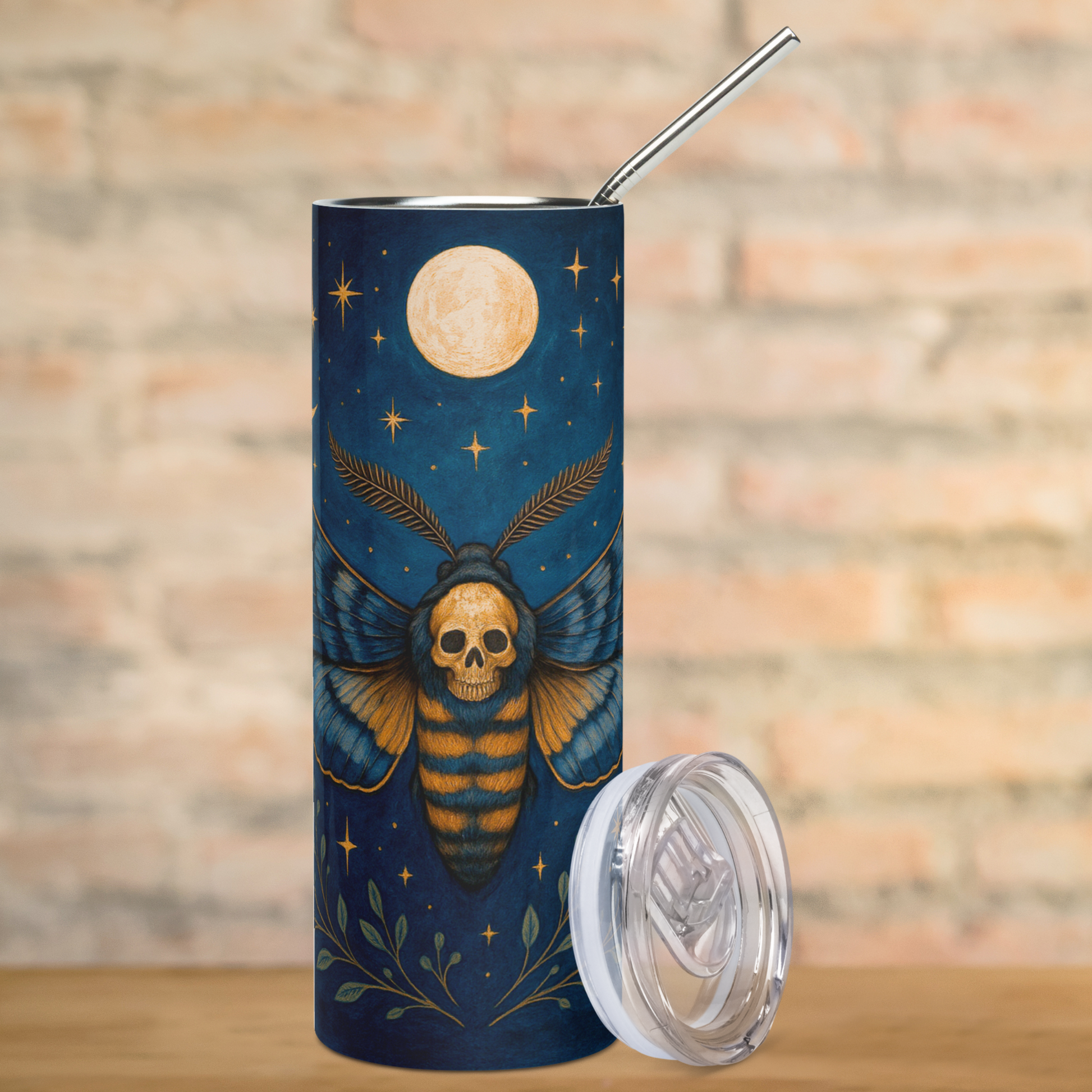 Death Head Moth Tumbler Stainless Steel 20 oz. View of front. Wings spread to each side with delicate feathered antennae the death head hawkmoth is shown in blues and golden browns with a gothic skull on the moth's back. Below the moth are spreading green branches. Above the moth is a full moon. Pagan Dark Cottagecore  Coffee Tumbler