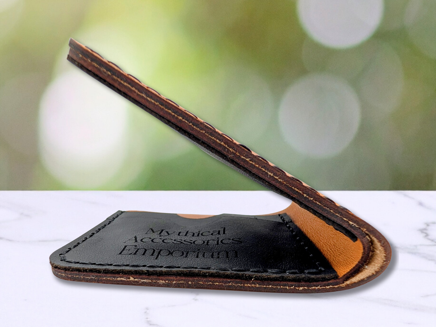 Leather Handmade Bi Fold Wallet. Folded edge view to see bottom edges of the wallet are dark. Bottom fold of the wallet shows the interior black leather card pockets with the Mythical Accessories Emporium engraved on the front of the card pocket.