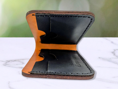 Edge View of the folded Leather Wallet to see into the wallet from the side. In this photo you see into the interior of the wallet to see all 4 card pockets made from black pebbled leather. The side on the counter has the logo engraved on the card pocket. There are two card pockets on each side of the wallet. Stitching is done in black waxed cord.
