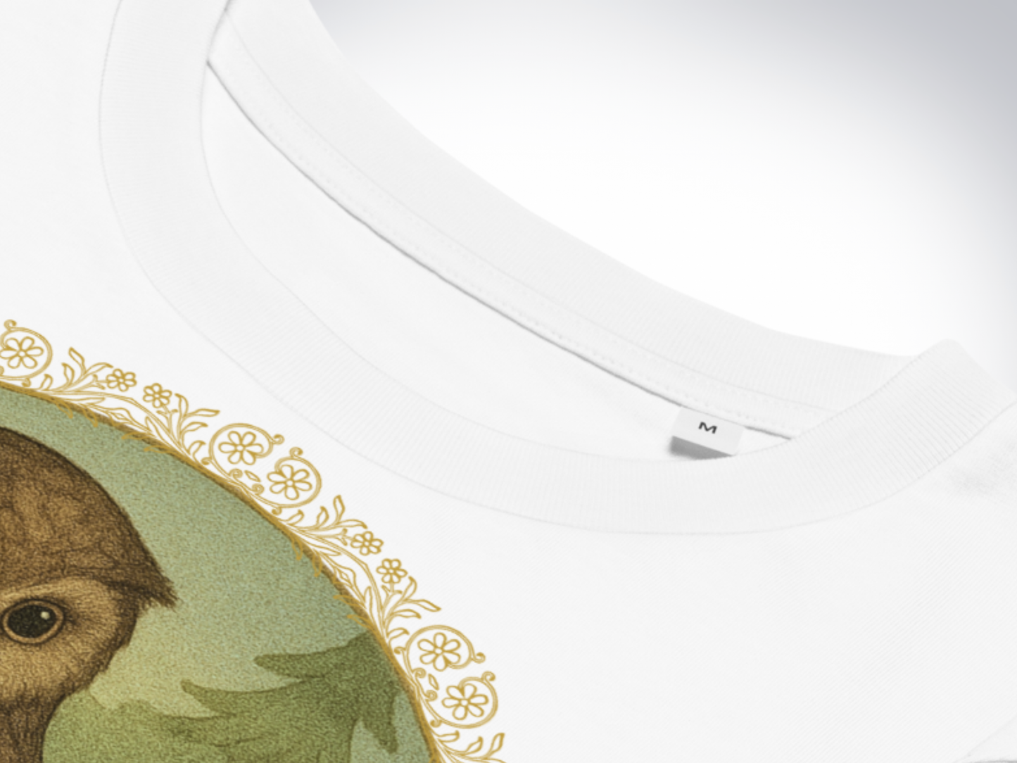 White tshirt close up to show the inside tape around the collar and the double needle stitching of the crewneck. You can see the gold floral border of the graphic and part of the top of the owl's head. with forest in the background. The graphic is in the shape of a circle.