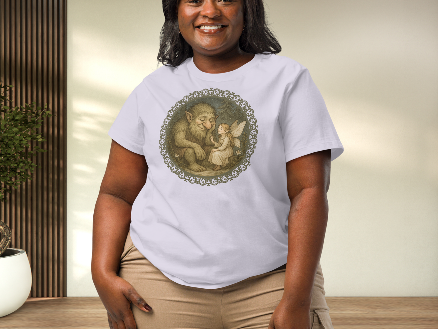 Curvy model wearing a lavender graphic tshirt. Graphic is in a circle. There is a frame of lattice lace. Inside the frame is a fairy/pixie sitting in the forest with a forest troll.
