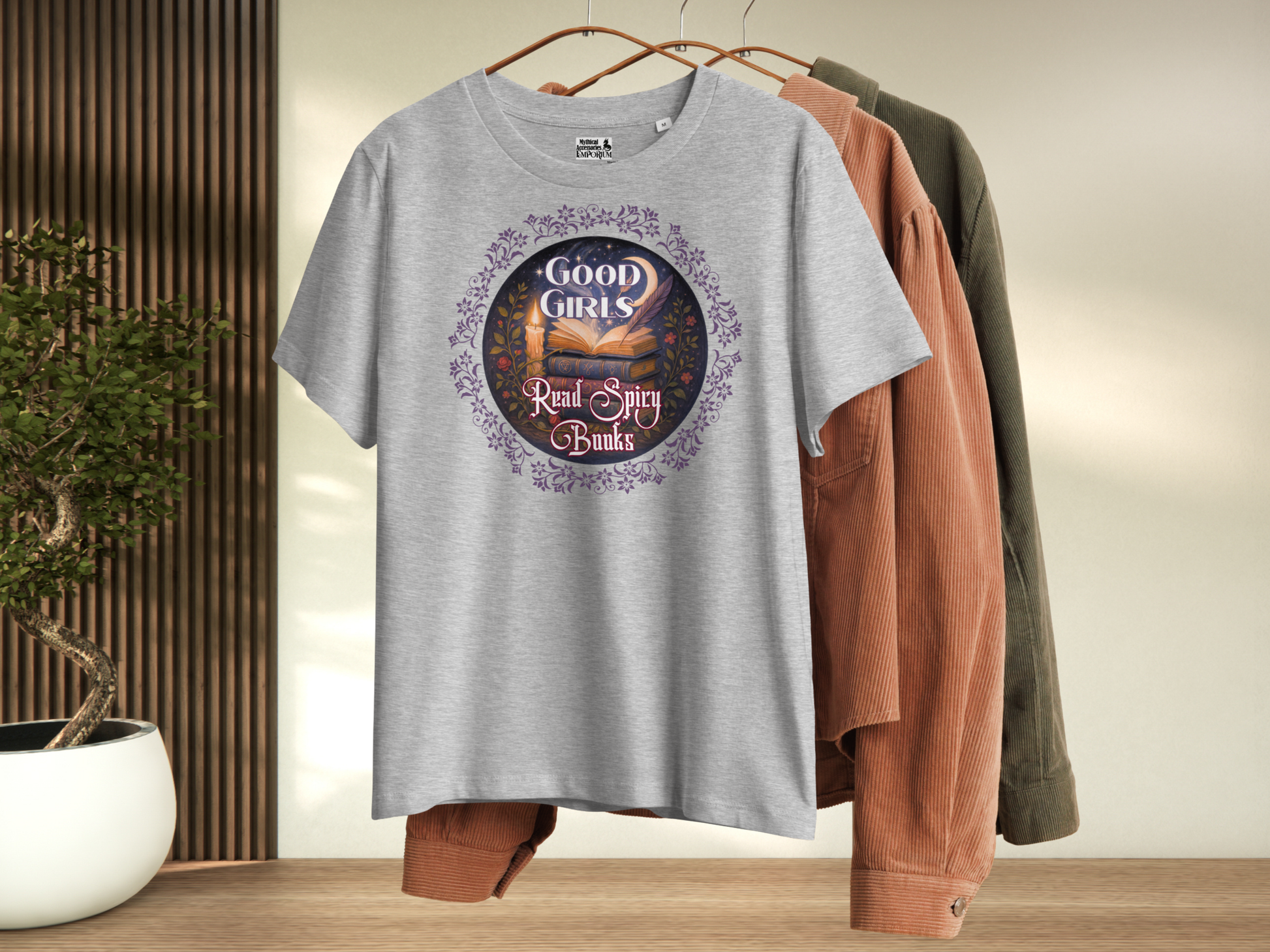 Athletic Grey Women's romantasy graphic tee on hanger, front view. Graphic has a purple floral frame around the circle graphic. The graphic has a botanical feel surrounding a stack of magic books with the top book open with light emanating from the book. A candle is lit nearby and a starry sky with a crescent moon is above the books. Above the books it states "Good Girls". Below the books it states "Read Spicy Books".