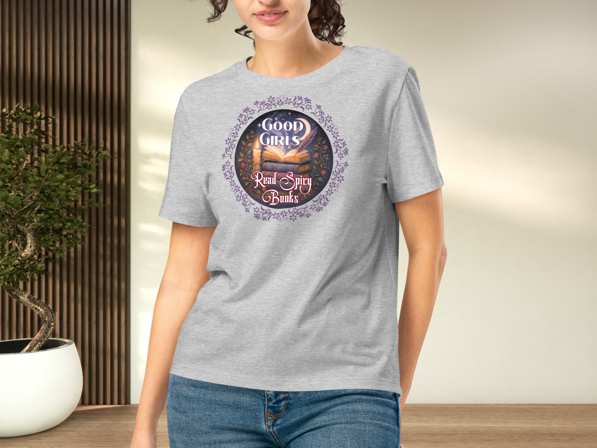 Model wearing a women's Romantasy Graphic Tee in Athletic Grey, front view. Graphic has a purple floral frame around the circle graphic. The graphic has a botanical feel surrounding a stack of magic books with the top book open with light emanating from the book. A candle is lit nearby and a starry sky with a crescent moon is above the books. Above the books it states "Good Girls". Below the books it states "Read Spicy Books".