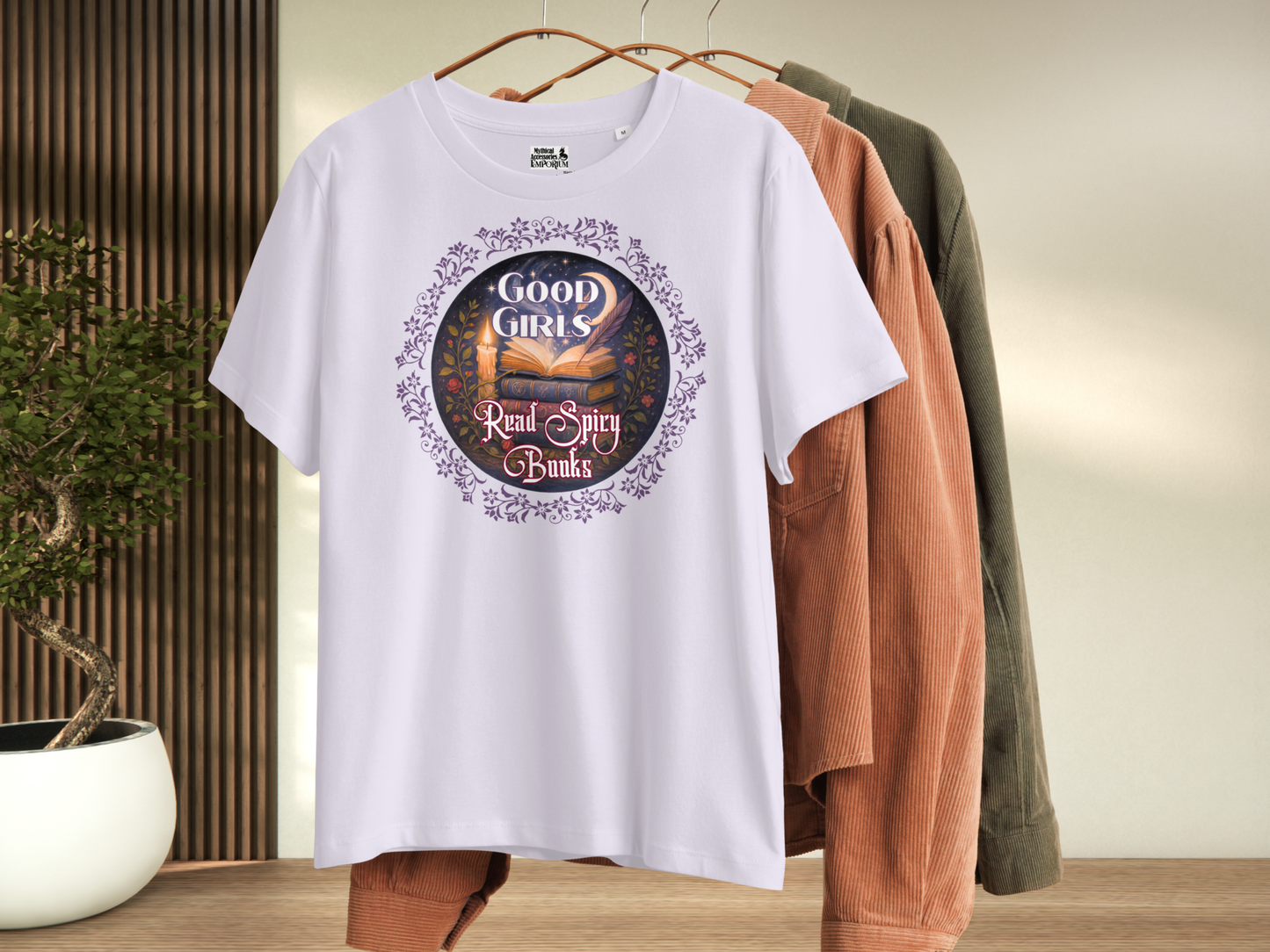 Lavender Women's Graphic Tee on Hanger, front view. Graphic has a purple floral frame around the circle graphic. The graphic has a botanical feel surrounding a stack of magic books with the top book open with light emanating from the book. A candle is lit nearby and a starry sky with a crescent moon is above the books. Above the books it states "Good Girls". Below the books it states "Read Spicy Books".