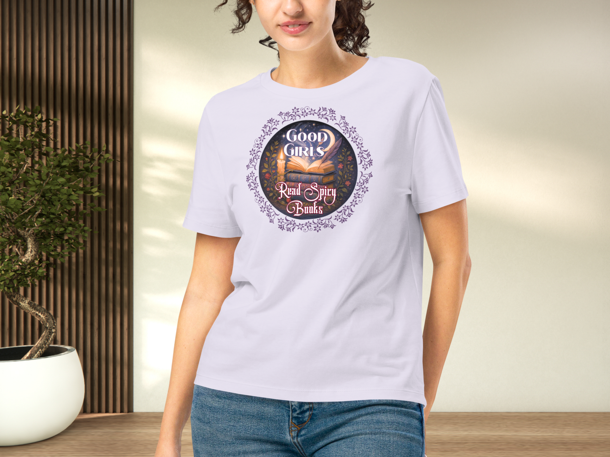 Model wearing a women's Romantasy Graphic Tee in lavender, front view. Graphic has a purple floral frame around the circle graphic. The graphic has a botanical feel surrounding a stack of magic books with the top book open with light emanating from the book. A candle is lit nearby and a starry sky with a crescent moon is above the books. Above the books it states "Good Girls". Below the books it states "Read Spicy Books".