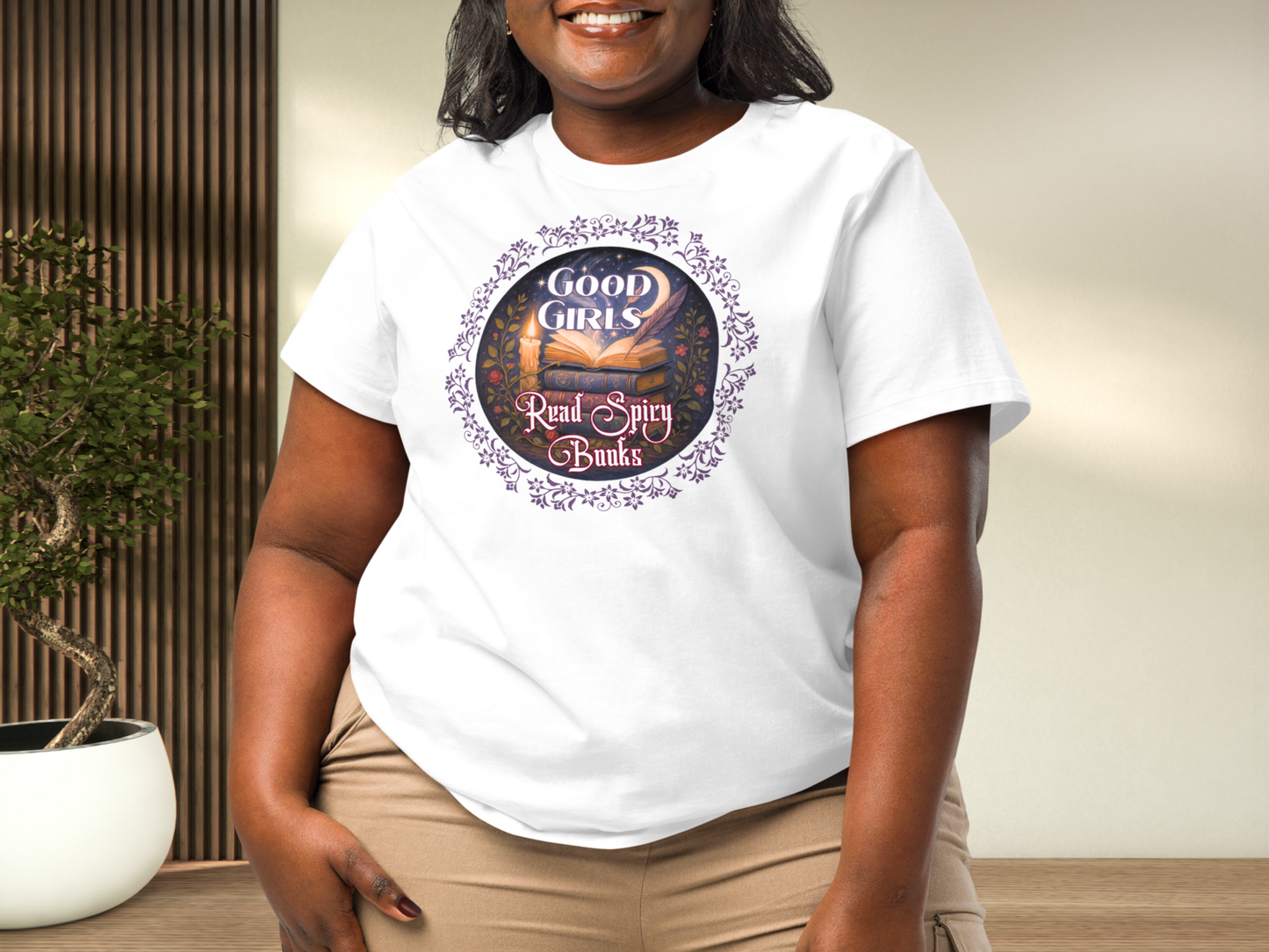 Curvy model wearing a women's Romantasy Graphic Tee in white, front view. Graphic has a purple floral frame around the circle graphic. The graphic has a botanical feel surrounding a stack of magic books with the top book open with light emanating from the book. A candle is lit nearby and a starry sky with a crescent moon is above the books. Above the books it states "Good Girls". Below the books it states "Read Spicy Books".
