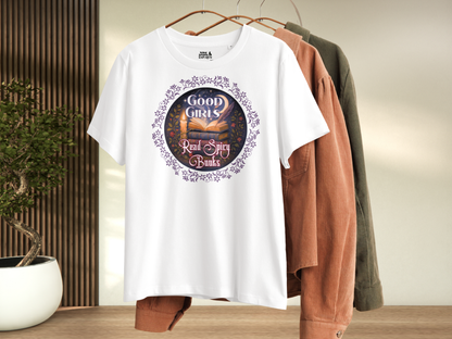 Hanging Romantasy Graphic Tee in White, front view. Graphic has a purple floral frame around the circle graphic. The graphic has a botanical feel surrounding a stack of magic books with the top book open with light emanating from the book. A candle is lit nearby and a starry sky with a crescent moon is above the books. Above the books it states "Good Girls". Below the books it states "Read Spicy Books".