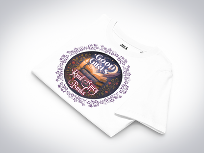 Romantasy Graphic Tee in white folded, front view. Graphic has a purple floral frame around the circle graphic. The graphic has a botanical feel surrounding a stack of magic books with the top book open with light emanating from the book. A candle is lit nearby and a starry sky with a crescent moon is above the books. Above the books it states "Good Girls". Below the books it states "Read Spicy Books".