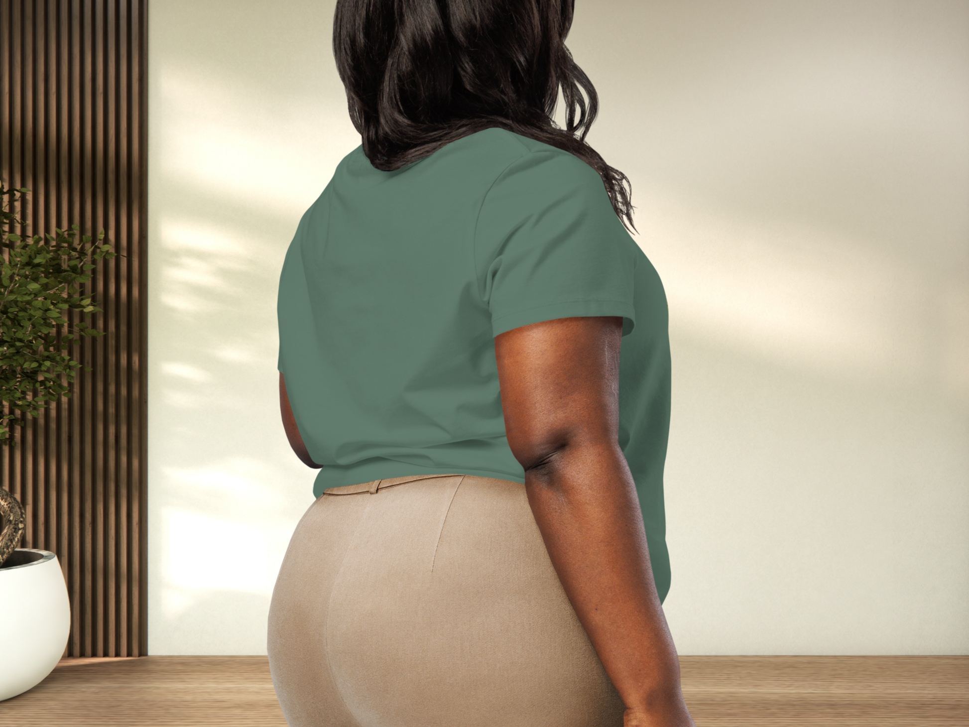 Person wearing a bay green shirt and beige pants in an indoor setting to show back view of tee and fit on a curvy model.
