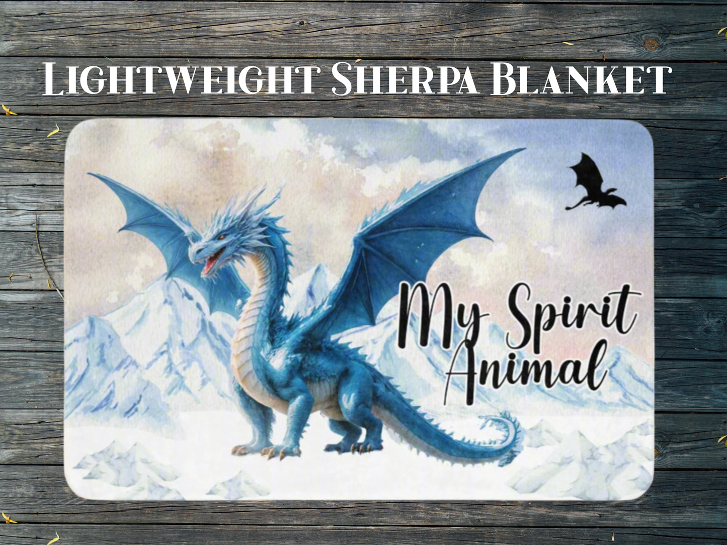 Throw Blanket with a blue dragon design and 'My Spirit Animal' text flat view laying on a wooden floor. This is a blue ice dragon with wings spread standing before snow and ice capped mountains. In the sky you see a black dragon silhouette.  Above the blanket you see the text, "Lightweight Sherpa Blanket".