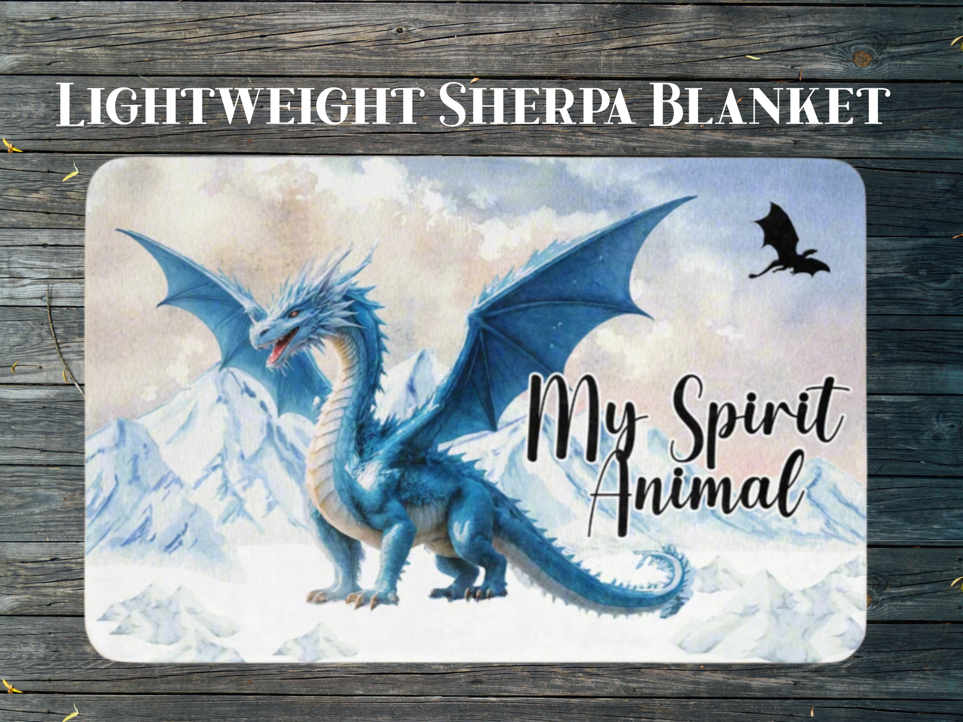 Throw Blanket with a blue dragon design and 'My Spirit Animal' text flat view laying on a wooden floor. This is a blue ice dragon with wings spread standing before snow and ice capped mountains. In the sky you see a black dragon silhouette.  Above the blanket you see the text, "Lightweight Sherpa Blanket".