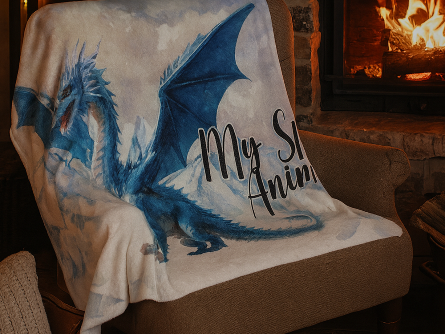 Blanket with a blue dragon design and 'My Spirit Animal' text draped over a chair in front of a fireplace.  This is a blue ice dragon with wings spread standing before snow and ice capped mountains. In the sky you see a black dragon silhouette.  Text to the right of the dragon is black with a white outline, "My Spirit Animal"