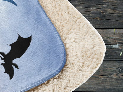 This image shows the ice dragon sherpa blanket folded over so that you see the front and the back corners. You can see the blanket is completely stitched all around and the corners are rounded and not pointed. The sherpa back piles against the front of the blanket laying over it. You see the soft blue background of the front against the natural beige color of the sherpa.