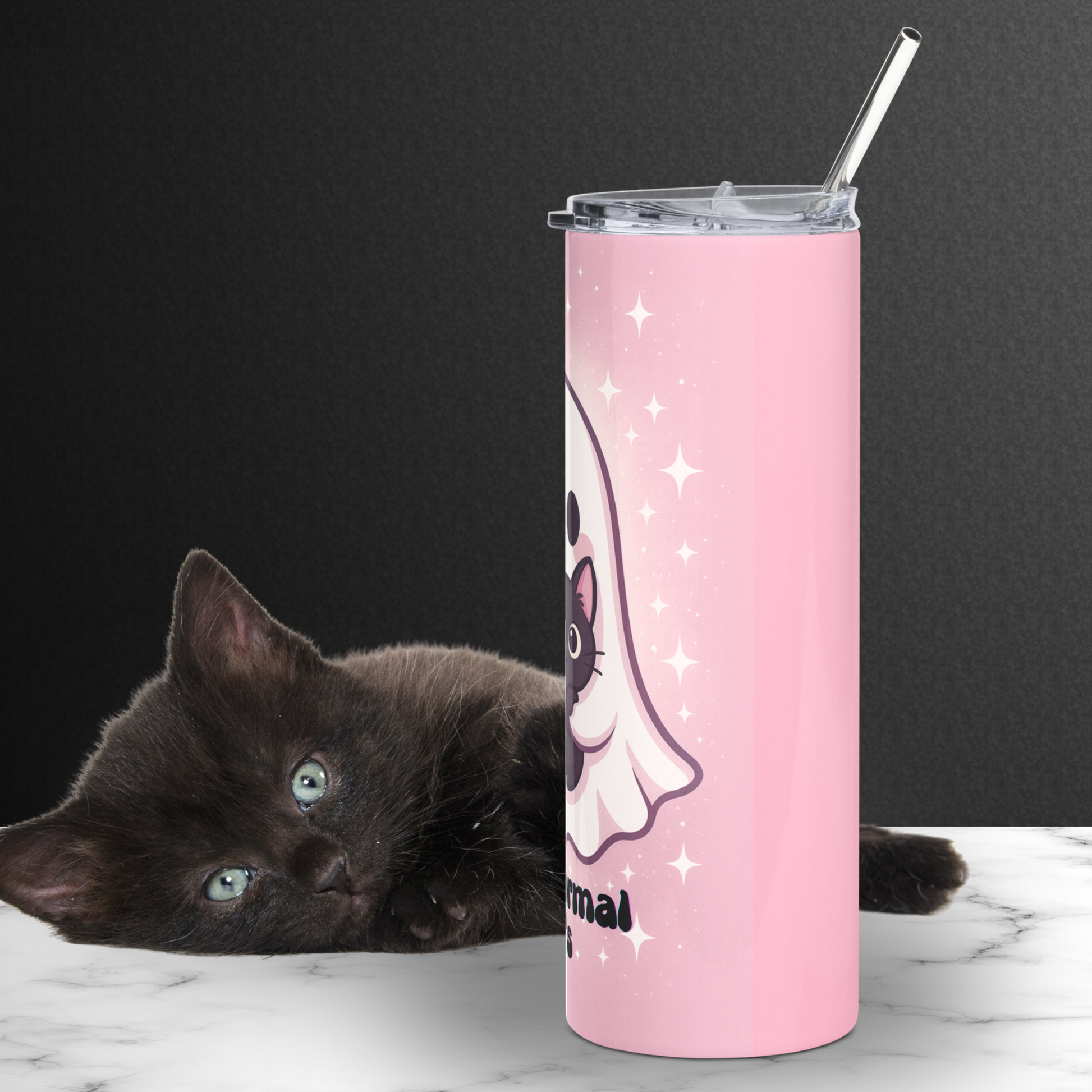 Pink Tumbler with a ghost holding a black cat right side view. Right side of ghost visible with an ear and eye of the cat. White stars surround the ghost for a sparkle effect. Metal straw is coming up out of the top of the tumbler. Behind the tumbler is a black kitten laying on the white counter. Spooky pink halloween black cat
