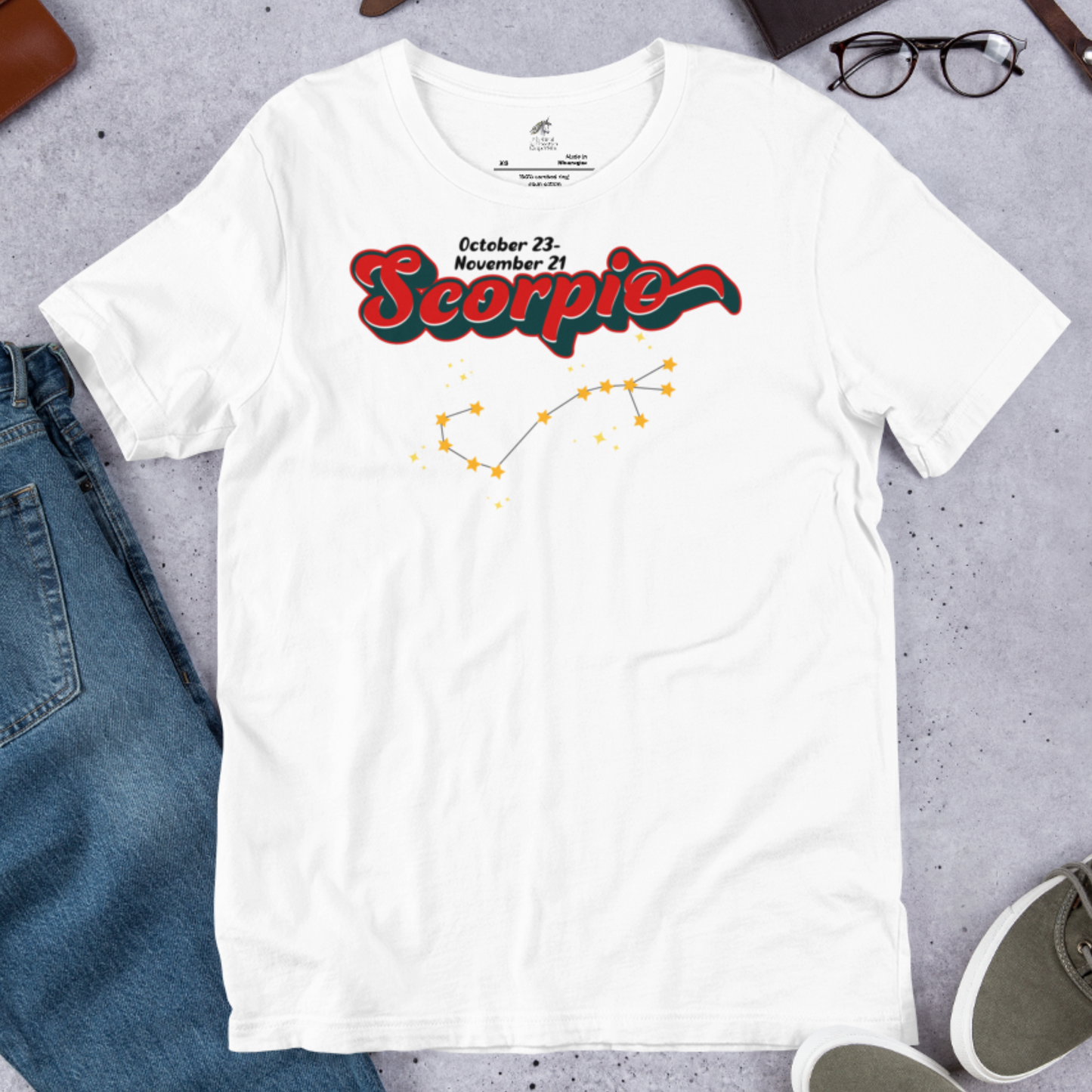 Front view of flat white men's Scorpio Tee. This astrology T-Shirt has the word Scorpio in large red script shadowed in black for a 3-D effect. Above  this it says October 23-November 21. Under Scorpio is the zodiac star constellation with yellow stars connected by a black line and lighter yellow smaller stars surrounding this. The perfect October or November Birthday Gift for him or yourself.