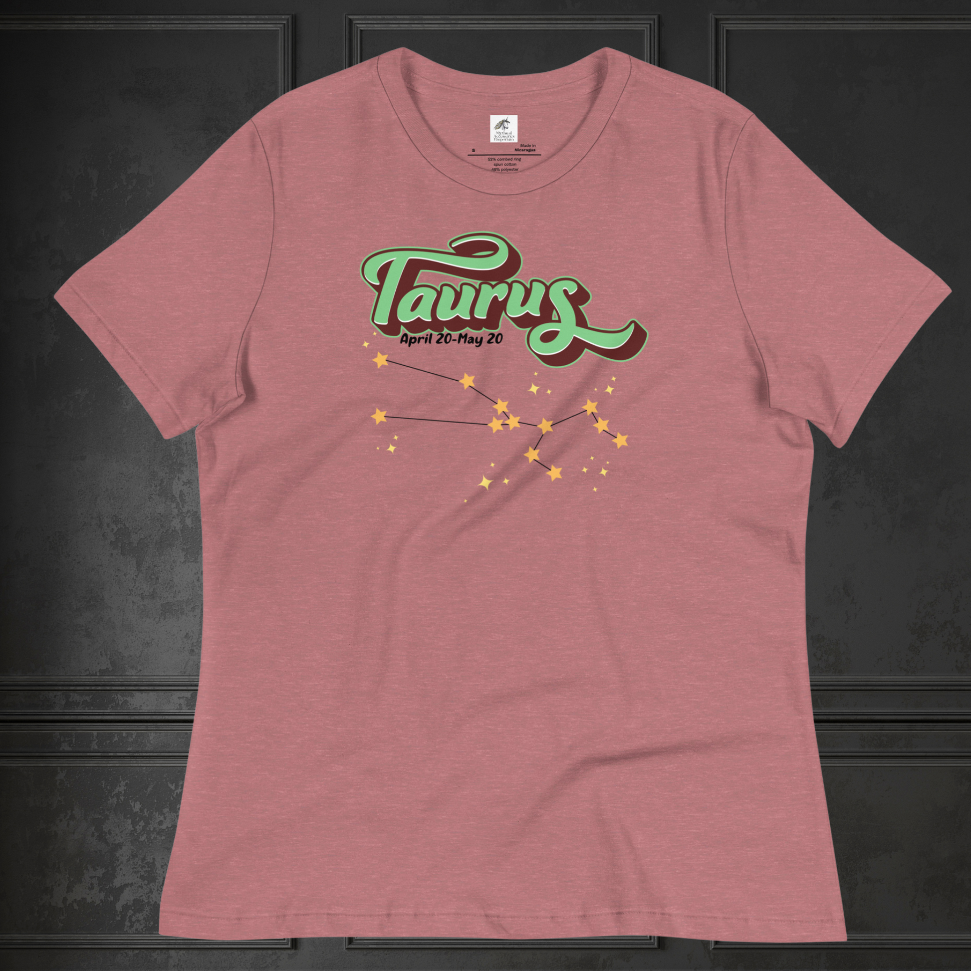 Front view of heather mauve Taurus Tee laying flat on a black surface. You can see the crew neck collar and short sleeves of the t shirt. This Astrology T-Shirt has the word Taurus in large leaf green script shadowed in deep brown for a 3-D effect. Below this it Says April 20-May 20. At the bottom is the star constellation for Taurus with yellow stars connected by a black line and  smaller stars surrounding the constellation. The perfect April or May Birthday Gift for Her or yourself.