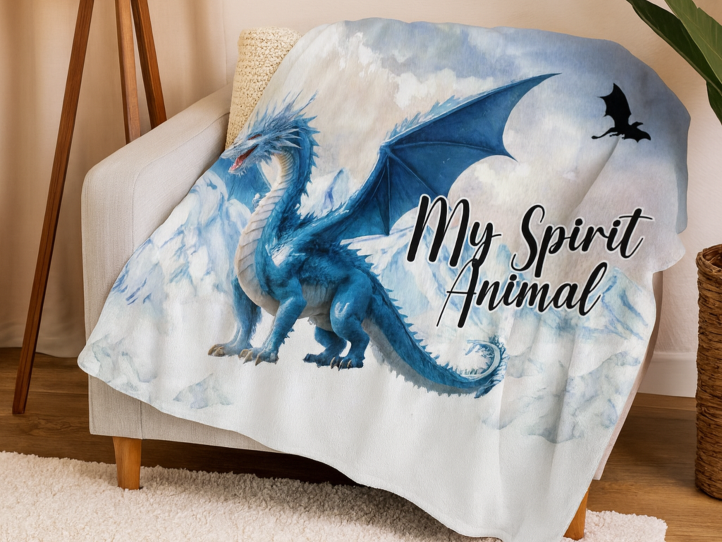 Throw Blanket with a blue dragon design and 'My Spirit Animal' text draped on a chair. This is a blue ice dragon with wings spread standing before snow and ice capped mountains. In the sky you see a black dragon silhouette. 