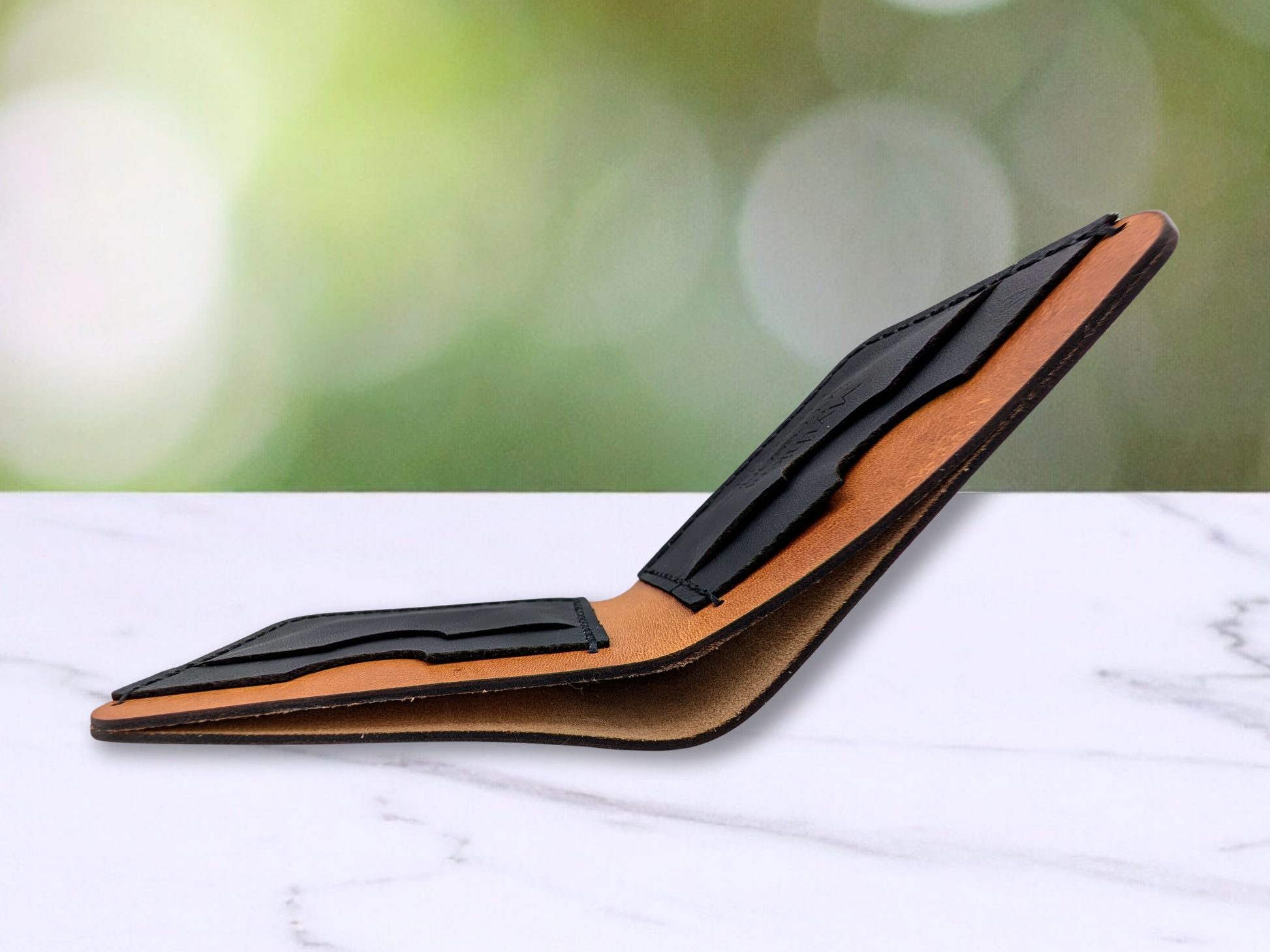 Wolf Leather Bi Fold Wallet laying unfolded. View is from the edge of the cash compartment. You can see into the cash compartment, dark edges of the light brown wallet, and into the tops of the black leather card pockets. 