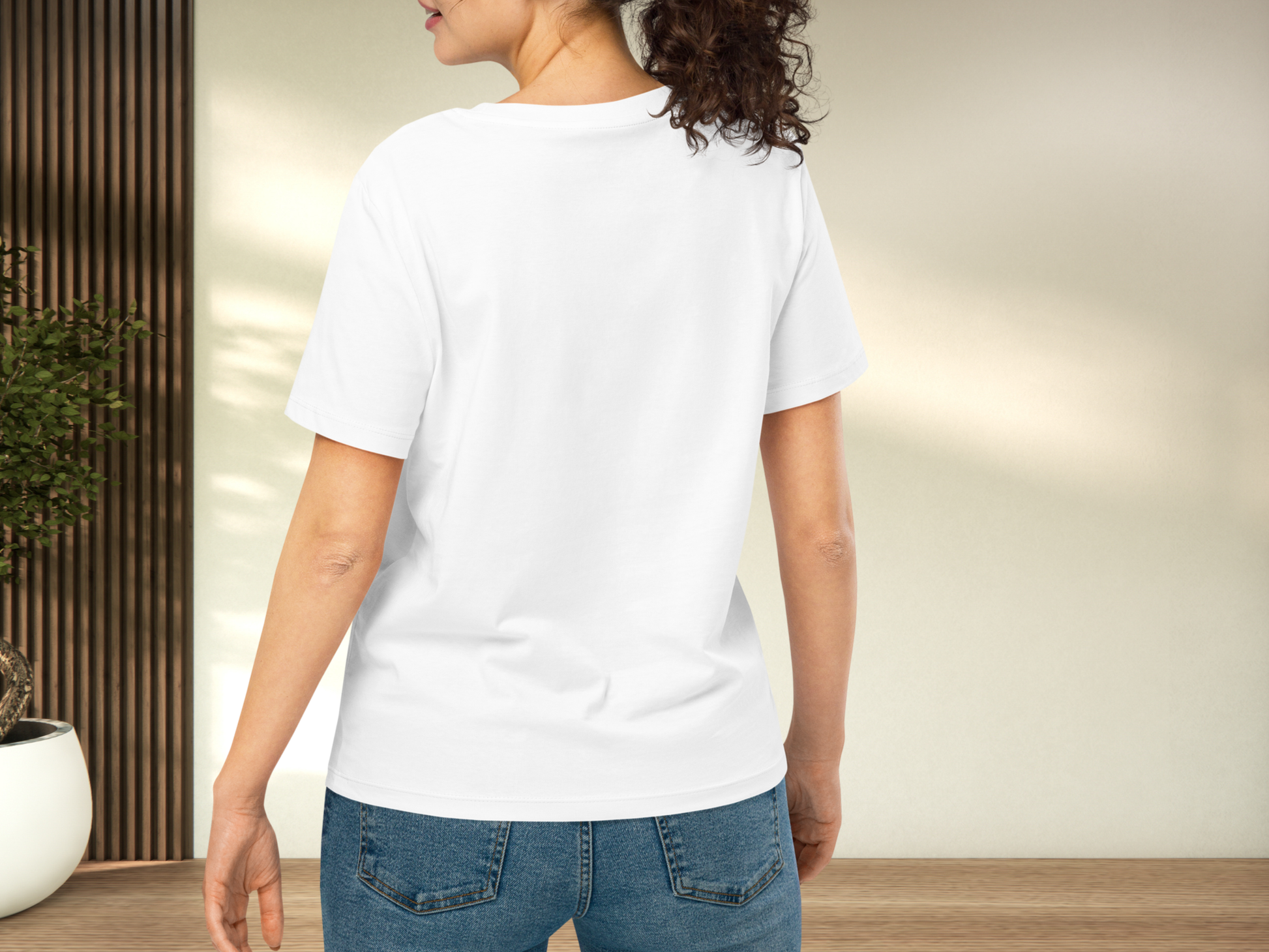 Back view of model wearing a white t-shirt and blue jeans. This view allows you to see both sleeves, the hem of the shirt hitting at mid hip and the back of the collar of the crewneck.