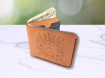 D20 veg tan wallet handmade with a D20 laser engraved on the front. The D20 is surrounded by leaves and a flower. This light brown leather bi fold wallet is dad style with cash peeking out of the cash compartment. You can see the wallet has been stitched with black waxed cording. You get a peak into the unfolded wallet at the black leather card pockets. 