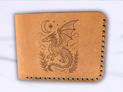 Front view of the folded bifold dragon leather wallet facing up. You see the stitching coming down the right side and the bottom of the wallet. The folded side is to the left. On the front is the laser engraved image of a flying dragon amongst the clouds with a crescent moon and a star above and below to each side is a vine of leaves. 
