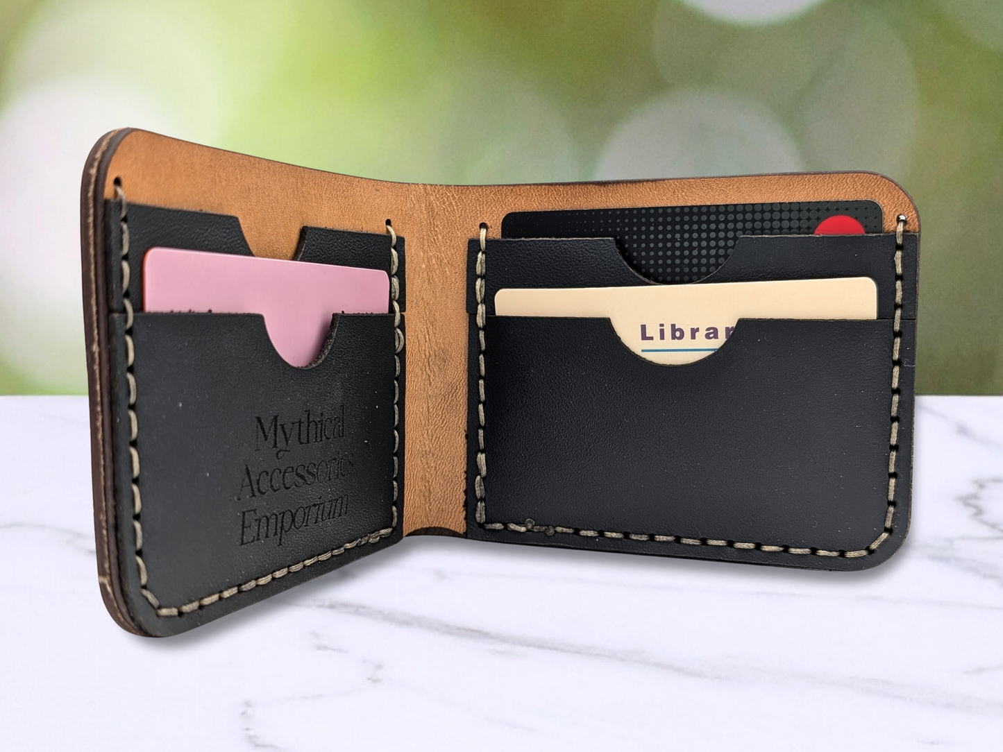 Dragon bi fold leather hand sewn wallet. This is an interior view of the wallet showing off the crease of the fold on the interior, the two black pebbled leather pockets on each side, the two layer thickness of the cash compartment and the dark edges of the leather can be seen. In this image you can see there are cards in the pockets to show the size.