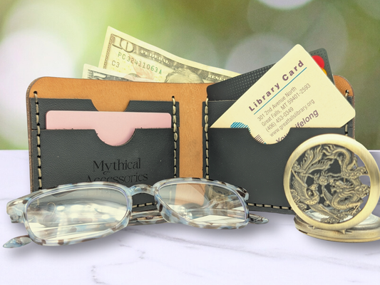 Open view of the dragon leather bifold wallet. Standing on it's side you are viewing the interior of the wallet. On both sides of the wallet you see two card pockets crafted out of black pebbled leather, the stitching can be seen holding the layers togethers. In each card pocket you can see a credit card or library card. Coming out of the top of the cash compartment you see a 10 and 5 dollar bill. To the front is a pair of glasses and a stopwatch for size comparison. 