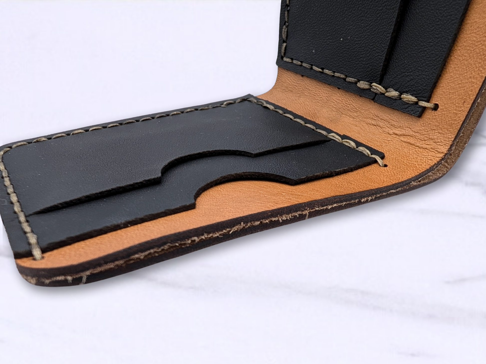 Bi fold handcrafted leather dragon wallet. The wallet is open with one of the sides back down on the white surface. You are looking from the top of the wallet down to see the double thickness of the veg tan leather forming the cash compartment. You can see the two layers of black pebbled leather forming the card pocket and how they are hand sewn together. 