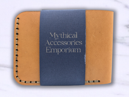 View of the dragon leather bi fold wallet. Here you are looking at the back of the wallet which is a smooth tan surface with stitching. The Mythical Accessories Emporium packaging in a dark blue stripe wraps around the back.