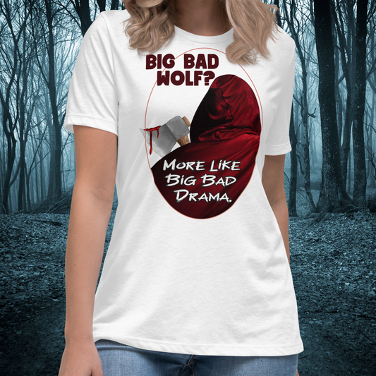 Red Riding Hood Women's Dark Fantasy T-Shirt. Front View White Graphic Tee on Model. Oval frame with thin red border. You can see the back of red riding hood with hood up. Bloody axe over her shoulder. Text Big Bad Wolf? More Like Big Bad Drama. Women's Feminist Bookish Shirt