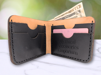 Open leather bifold wallet with money and cards on a marble surface. You see a 10 and 5 dollar bill sticking up out of the cash compartment of the open wallet that is standing up. You are seeing the interior view. There are two card compartments on each side of the wallet with notches to make it easier to pull the cards out of the pockets. The card pockets are hand sewn of black pebbled leather with black stitching onto veg tan leather. On the right side bottom of the card pockets you see the logo