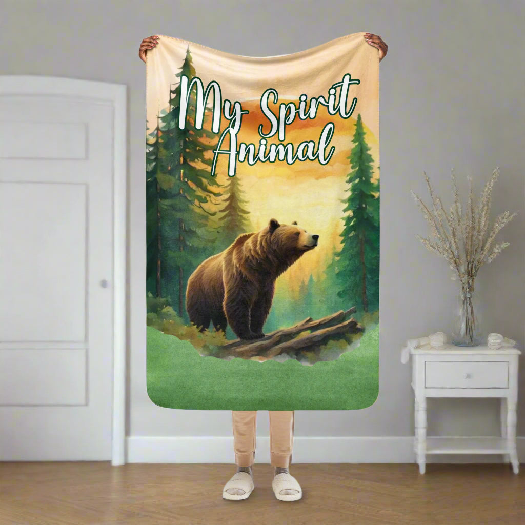 My Spirit Animal bear sherpa blanket.  Front view of size 37"x57" bear blanket. Model is holding blanket up in the air. This is a children's or a travel size blanket. Grizzly Bear paused in front of logs walking through the forest framed in a sunset. My Spirit Animal text at the top in white script.