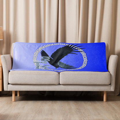 My Spirit Animal Raven Crow Sherpa Blanket. Front View of blanket shown over the back of a loveseat, size 37"x57". Raven wings spread as he soars inside a white Celtic Knot circle frame, My Spirit Animal bisects the lower right side of the circle.  Background of blanket is a dip dyed deep violet blue. Darker at the top  with a graduated color to the lighter bottom. Mythical Accessories Emporium. the crow shirt, Morrigan, Celtic Mythology, Odin's Ravens, WIccan