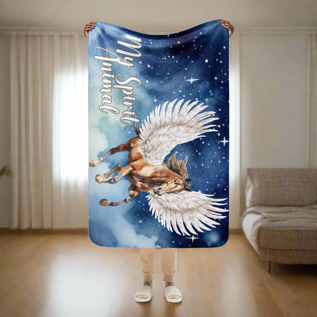 My Spirit Animal Pegasus Sherpa blanket. Women holding a blanket up over her head size 37"x57". This blanket is perfect for children or as a travel blanket. Pegasus white feathered wings on a Pinto with a dark brown mane and tail, galloping through the sky against a background of clouds and stars. Mythical Accessories