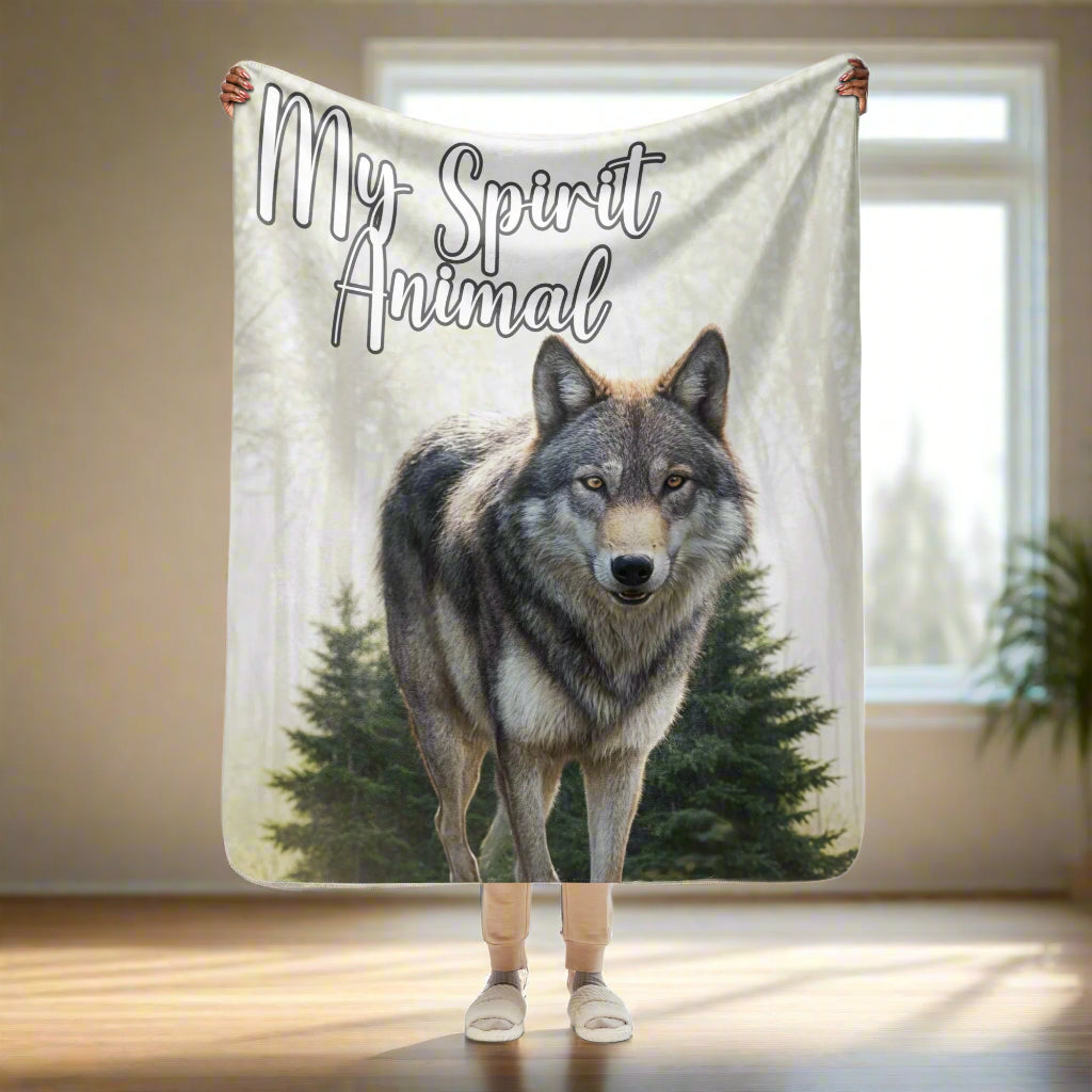 Wolf Sherpa Blanket My Spirit Animal. Front view held up by model size 50"x60", standard couch throw size. A grey timberwolf gazes out at you from the forest. Behind the wolf is a stand of pine trees. Behind these in the fog ar more trees. Upper left corner in white with a black outline My Spirit Animal.