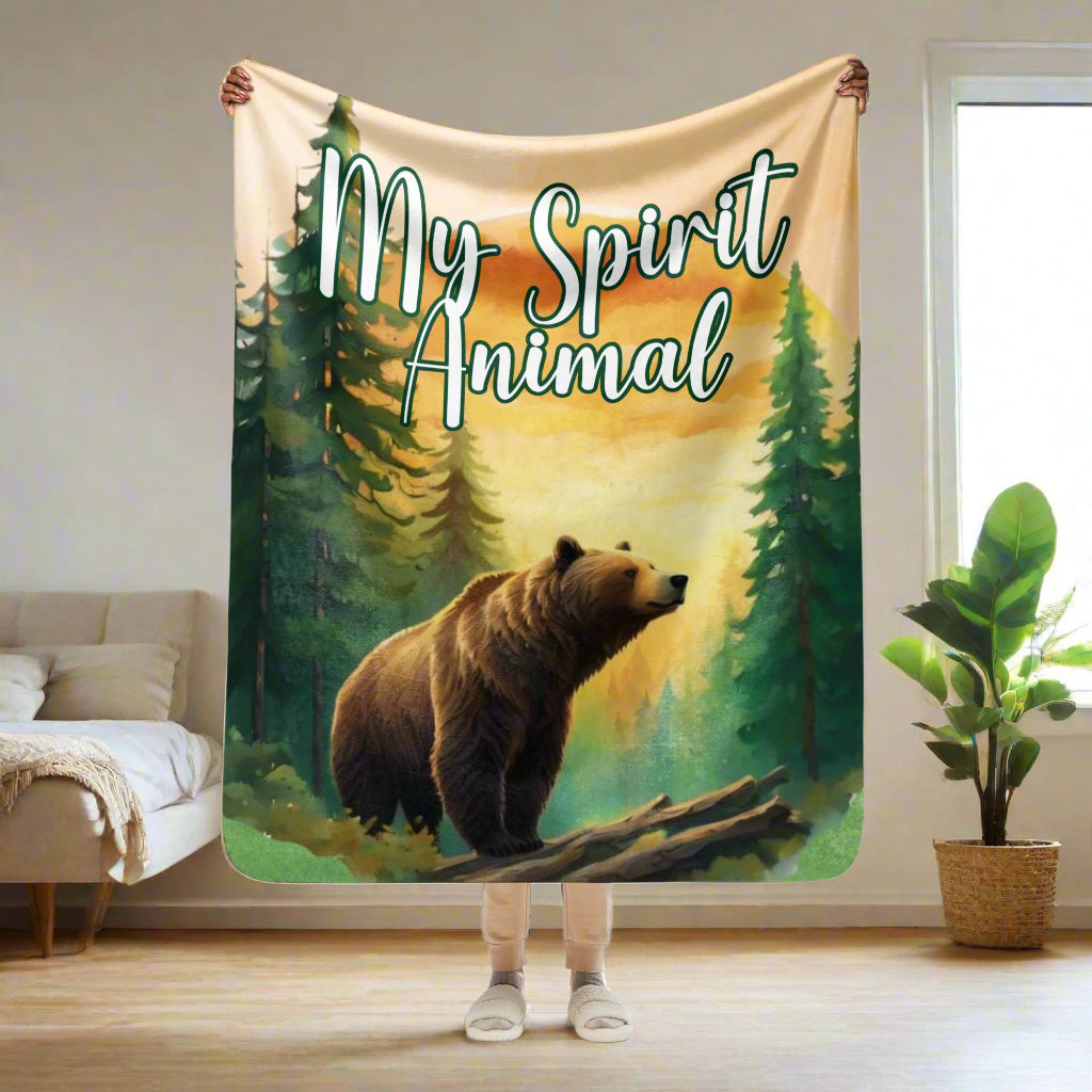 My Spirit Animal bear sherpa blanket.  Front view woBlanket men holding blanket up in her hands 50"x60". This is a normal size throw blanket or a couch throw.  Grizzly Bear paused in front of logs walking through the forest framed in a sunset. My Spirit Animal text at the top in white script