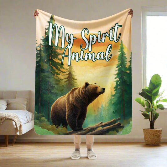 My Spirit Animal bear sherpa blanket.  Front view model holding blanket up in her hands 50"x60". This is a normal size throw blanket or a couch throw. Grizzly Bear paused in front of logs walking through the forest framed in a sunset. My Spirit Animal text at the top in white script